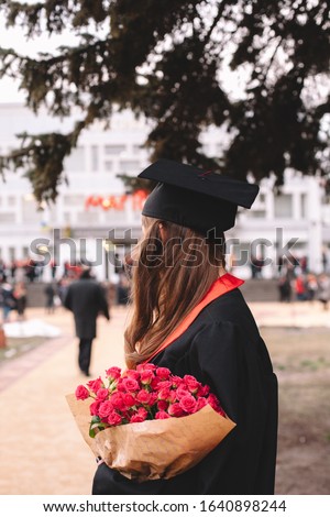 Rear view of female graduate student in graduation gown holding bouquet of flowers while standing in campus at graduation ceremony Royalty-Free Stock Photo #1640898244
