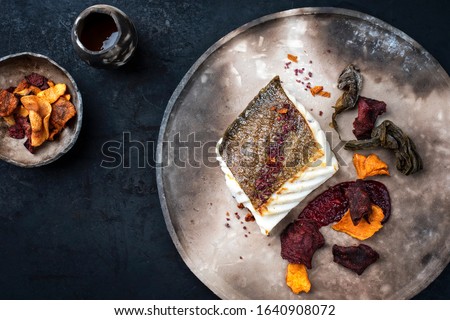 Gourmet fried European skrei cod fish filet with algae and vegetable crisps as top view on a modern design plate 