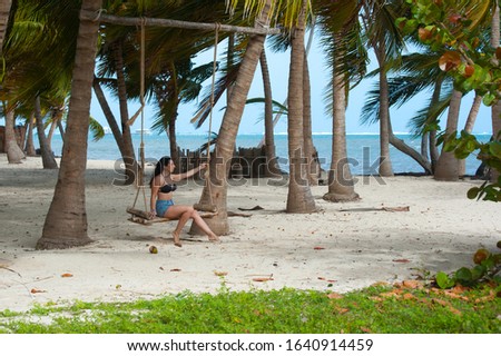 Brunette young woman sitting in the swing on the beach shore with palm trees