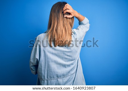 Middle age beautiful woman wearing casual shirt standing over isolated blue background Backwards thinking about doubt with hand on head