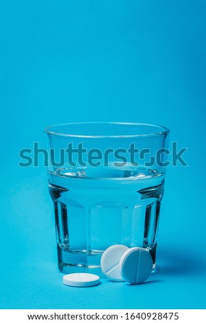 Close up of painkiller tablet in glass of water over blue background