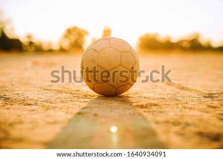 Silhouette golden hour moment of an old ball for street soccer football under the sunset ray light at the countryside field. Picture with copy space.