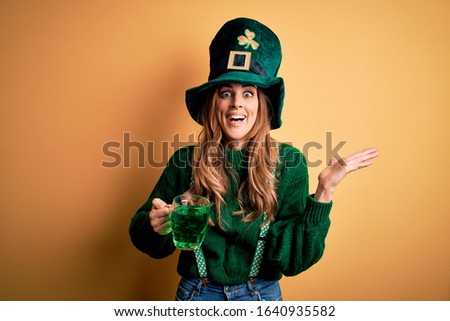 Beautiful woman wearing hat drinking jar of green beverage celebrating saint patricks day very happy and excited, winner expression celebrating victory screaming with big smile and raised hands