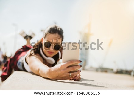 Let's take a selfie. A woman lies by the beach and uses a cell phone