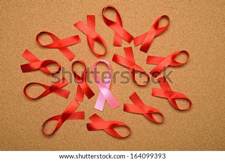 Pink ribbon between red ribbon on corkboard. Breast cancer awareness concept