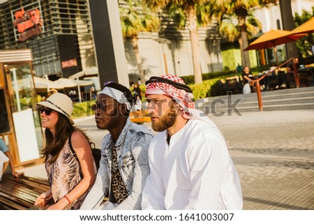 A European woman , an African-American and an Arab man sit on a bench and look into the distance