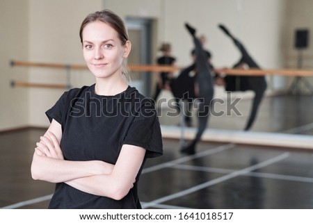 Horizontal medium portrait of young woman wearing black T-shirt standing with arms crossed in rehearsal studio looking at camera