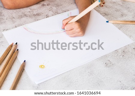 The child's hands are painted with colored pencils on a white paper on a gray table.
