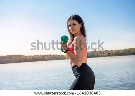 young beautiful girl is engaged in morning gymnastics with dumbbells at the lake