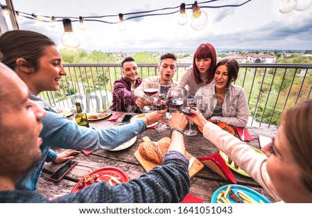 Wide angle view of happy people toasting red wine together at rooftop party in open air villa - Young friends eating bar-b-q food at restaurant patio - Cool friendship concept on warm vivid filter