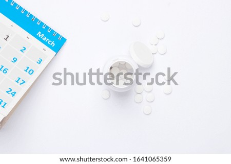 Bottle pills with desktop calendar on white background. top view