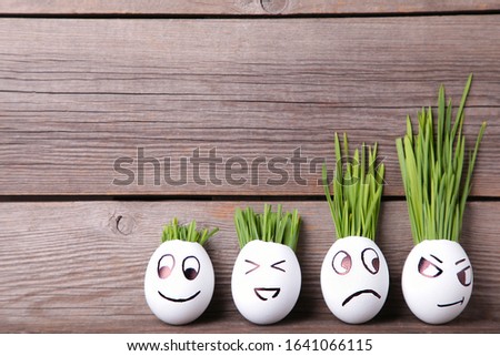Funny handmade eggs with hair of green grass with copy space. Easter concept on grey wooden backgrund, top view