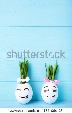 Funny handmade eggs with hair of green grass with copy space. Easter concept on blue wooden backgrund, top view