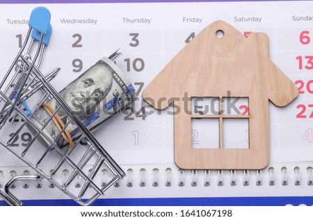 Payment of rent for housing. Mini house figurine, shopping trolley on calendar.