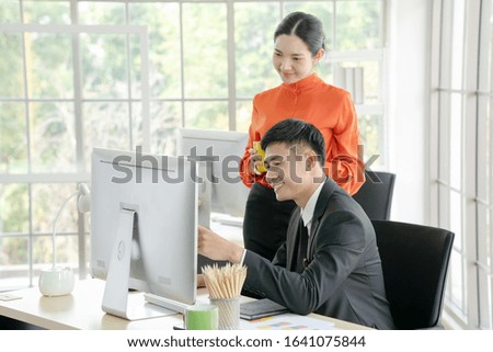 Two business people working together on computer. Businessman and businesswoman looking at computer monitor in office.