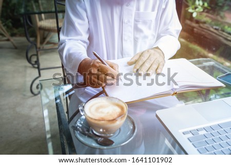 Young handsome businessman arab muslims in coffee shop wearing hijab dressed  write on book file with laptop on table.focus on hand.