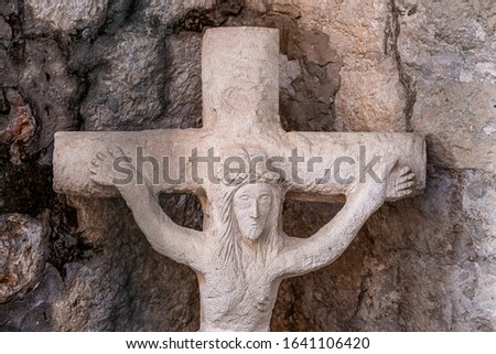 Closeup ancient statue of Jesus Christ and the crucifixion made of gray stone, cracked brick wall background