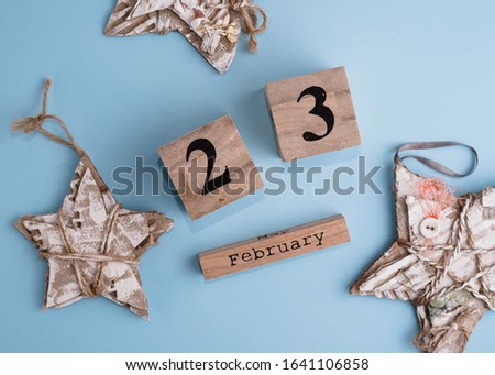 Content February 23. Date February 23 on a wooden calendar and handmade paper stars on a blue background
