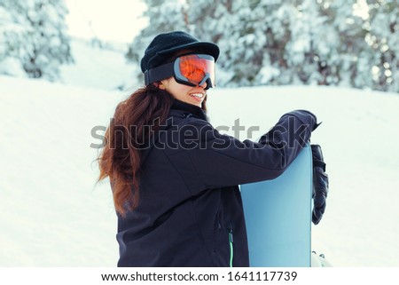 Stock photo of a young girl laughing while holding her snowboard on a snowy mountain