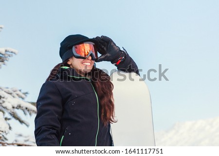 Stock photo of a young girl holding her snowboard and glasses on a snowy mountain