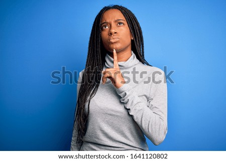 Young african american woman standing wearing casual turtleneck over blue isolated background Thinking concentrated about doubt with finger on chin and looking up wondering