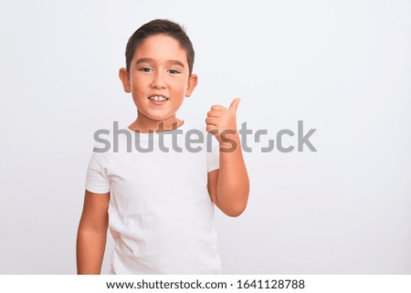 Beautiful kid boy wearing casual t-shirt standing over isolated white background doing happy thumbs up gesture with hand. Approving expression looking at the camera showing success.