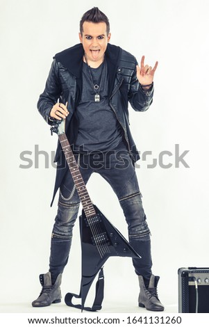 Rebellious guitar player showing horn sign while sticking out tongue and looking at camera. 