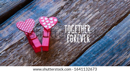 Two clothespins hearts lie on a wooden table. Lettering together forever. Love