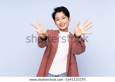 Young Asian girl over isolated blue background counting seven with fingers
