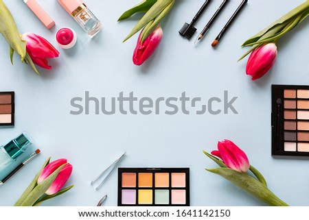 Decorative cosmetic set and beautiful pink tulips on trendy blue background with copy space for your text. Creative spring make up concept.