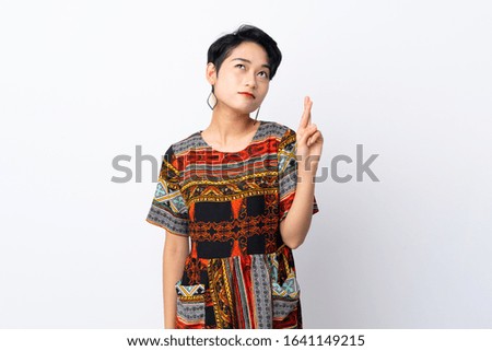 Young Asian girl with a colorful dress over isolated white background with fingers crossing and wishing the best