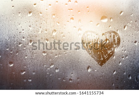 Heart painted on glass in Rainy weather, is fogged up and there are many drops on it, in a romantic pink tint, sunny sunset