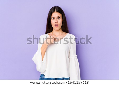 Young caucasian woman isolated on purple background surprised pointing with finger, smiling broadly.