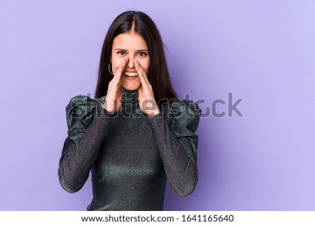 Young caucasian woman isolated on purple background saying a gossip, pointing to side reporting something.