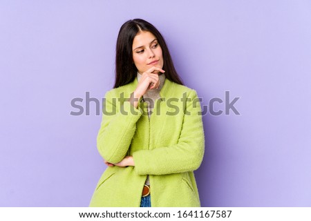 Young caucasian woman isolated on purple background looking sideways with doubtful and skeptical expression.
