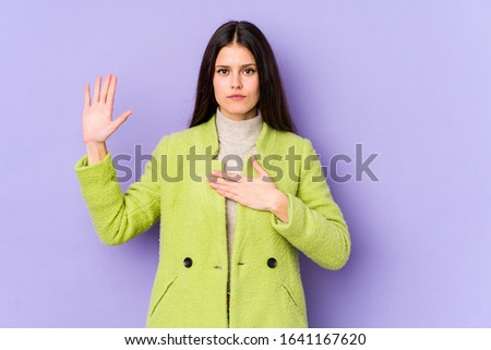 Young caucasian woman isolated on purple background taking an oath, putting hand on chest.
