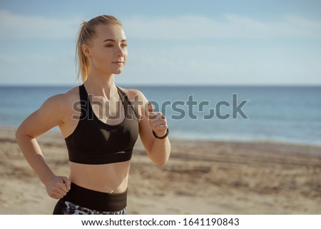 woman running seaside with sport clothers ans smart watches on hand; female jogger waist-high view training; sport and fitness concept.