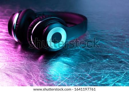 Retro 90s style photo of black stylish wireless headphone in neon lights.