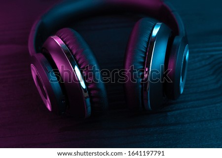 Black headphone on dark wooden background. Stylish wireless headset in neon light.