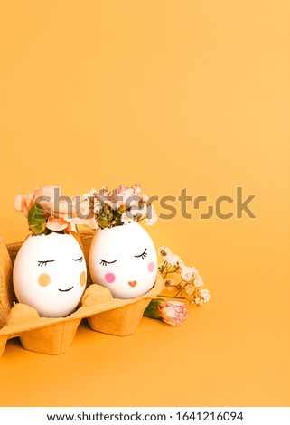 Easter creative concept. Easter decorative eggs with painted cheerful faces and flowers instead of hair in the cardboard egg tray on the yellow background. Copy space, close up.