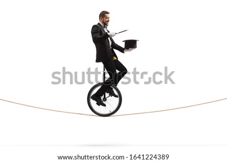 Magician holding a wand and a hat and riding a unicycle on a rope isolated on white background