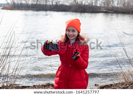 Girl dressed in red jacket, poses for making selfie or photo of herself with smartphone. People and leisure concept. Girl makes selfie in a red jacket.Girl 9 years old with a smartphone in her hands.