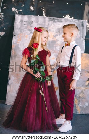 boy gives the girl in a gorgeous red rose dress and red heart-shaped balloons. Valentine's Day. Blonde hair kids.