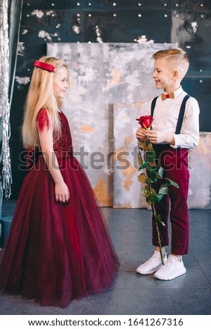 boy gives the girl in a gorgeous red rose dress and red heart-shaped balloons. Valentine's Day. Blonde hair kids.