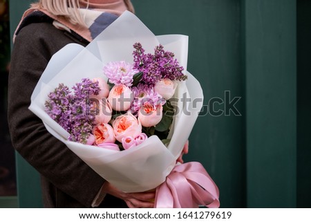 Spring flowers mix assorted bouquet in pink paper in woman hands background.