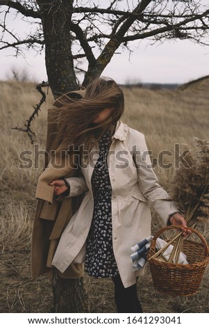 Portrait of a girl posing fashion in the autumn in the dry field. Dressed in neutral clothes.
The wind blows the hair of the lady.
Loneliness, suffering and depression.
Retro style editing.
