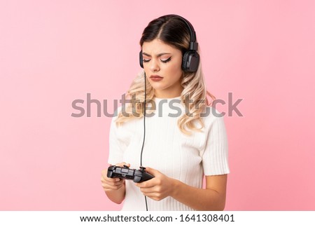 Teenager girl over isolated pink background playing at videogames