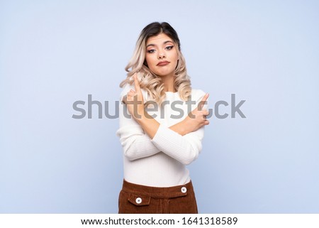 Young teenager girl over isolated blue background pointing to the laterals having doubts
