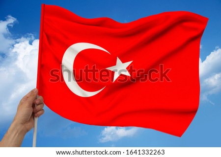 male hand holds against the background of the sky with clouds the national flag of Turkey on a luxurious texture of satin, silk with waves, closeup, copy space, concept of travel, economy, politics