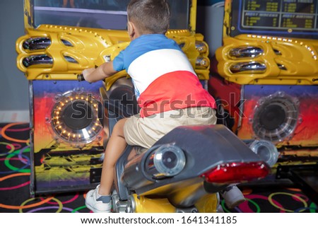 boy on a children's computer motorcycle, a gaming machine for children, developing computer technologies. kid boy playing arcade video game. Motorcycle Racing . Kid playing motorbike simulator .